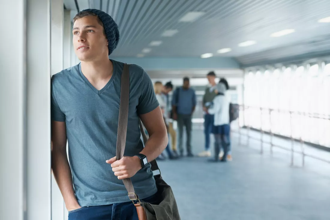 Student z plecakiem stoi przy oknie na korytarzu uczelni