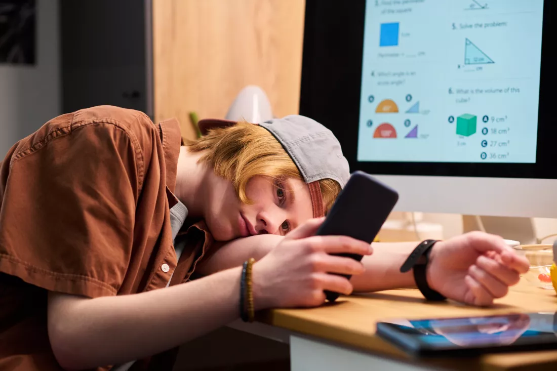 teenage-boy-holding-smartphone-while-avoiding-online-math-study