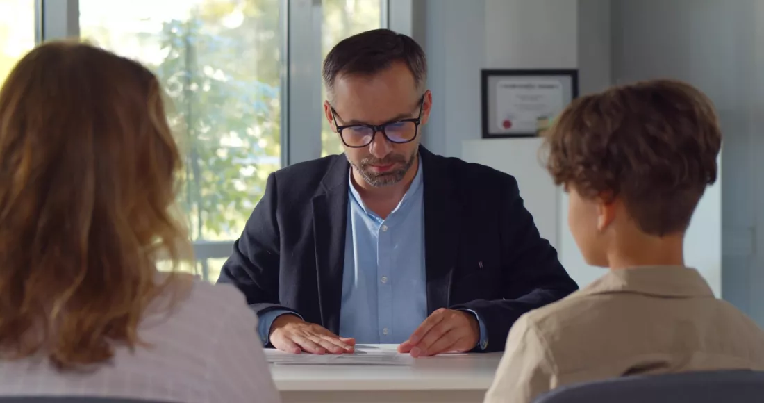 Matka z synem rozmawiaja z dyrektorem szkoly w gabinecie