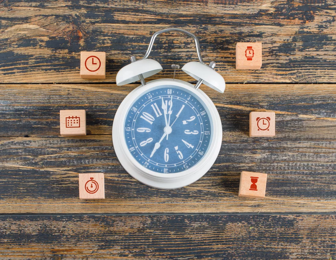 time-management-concept-with-wooden-blocks-with-icons-big-clock-wooden-table-flat-lay